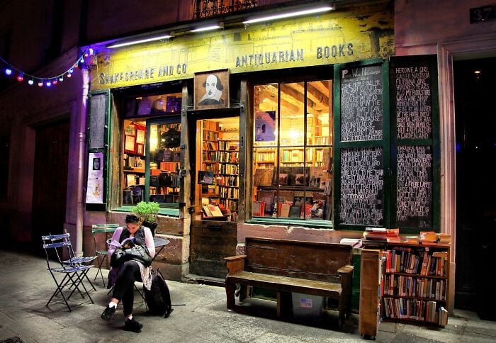 Libreria accogliente e grandiosa di notte con illuminazione calda, piena di libri e una persona che legge fuori. Libreria accogliente e grandiosa di notte con illuminazione calda, piena di libri e una persona che legge fuori.