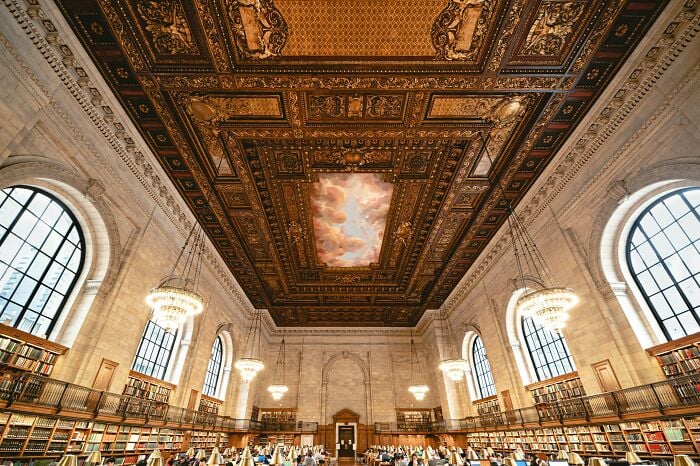 Interno di una grandiosa biblioteca con soffitto ornato, grandi finestre ad arco, lampadari e file di scaffali pieni di libri. Interno di una grandiosa biblioteca con soffitto ornato, grandi finestre ad arco, lampadari e file di scaffali pieni di libri.