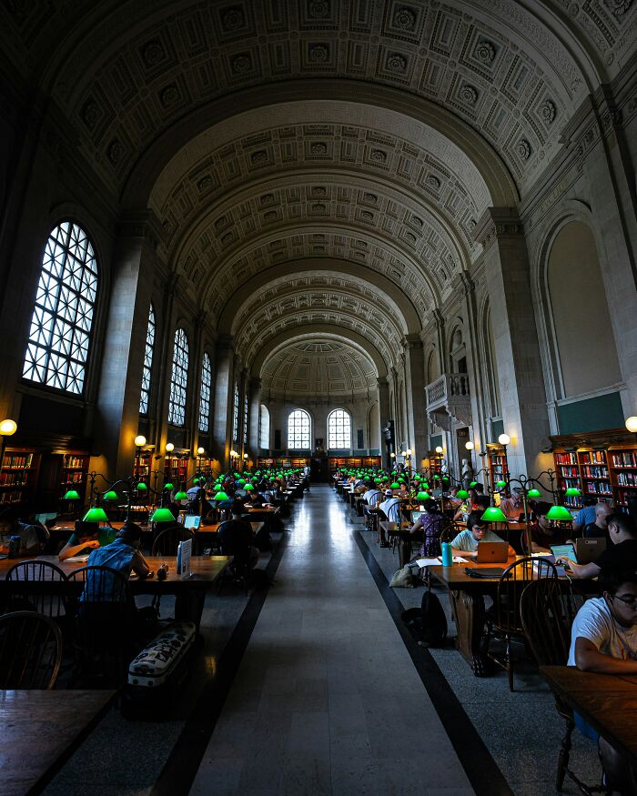 Grandiose library interior with high arched ceilings, large windows, and rows of study tables with green lamps and readers. Grandiose library interior with high arched ceilings, large windows, and rows of study tables with green lamps and readers.