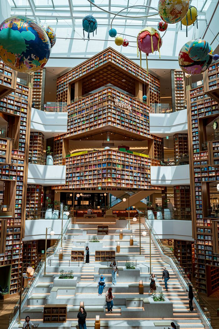 Grandiose library interior with towering bookshelves, large skylight, and colorful planet sculptures hanging from ceiling. Grandiose library interior with towering bookshelves, large skylight, and colorful planet sculptures hanging from ceiling.